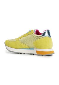 Žluté semišové tenisky se stříbrnými akcenty, modrými a oranžovými detaily, texturovaným svrškem a bílou gumovou podrážkou. Boční pohled ukazuje šněrování.