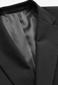 Blazer noir avec une doublure intérieure en satin gris lisse, montrant les détails du col et du revers.
