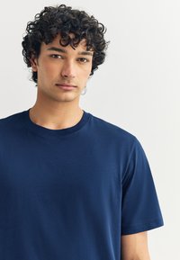 Tmavomodré tričko s krátkym rukávom vyrobené z mäkkej látky, s okrúhlym výstrihom a jednoduchým, bezšvovým dizajnom bez viditeľných log.