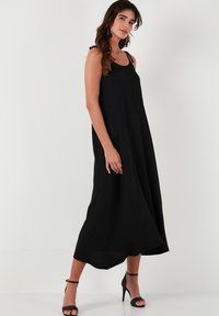 Schwarzes, fließendes Maxikleid aus leichtem Stoff mit dünnen Trägern. Hat eine entspannte Silhouette und eine leicht strukturierte Oberfläche.