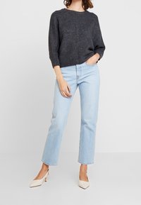 Grå lättstickad tröja med trekvartsärmar, i kombination med ljusblå raka jeans och krämfärgade pumps med spetsig tå.