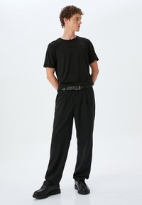 Sort t-shirt, afslappet pasform; parret med højtaljede sorte bukser, der har et bælte. Klodsede sorte støvler fuldender outfittet. Minimalistisk design.