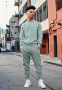 Felpa verde menta abbinata a pantaloni jogger, caratterizzata da una vestibilità casual, vita con cordino e accenti di logo bianchi. Indossata con sneakers bianche.