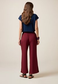 Navy blue top with rolled sleeves; loose maroon wide-leg pants; black flat sandals; wrist bracelet; smooth texture, relaxed fit.
