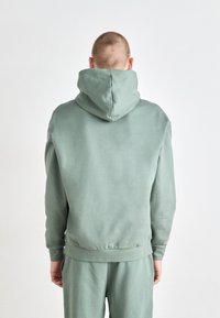 Sudadera con capucha en un verde apagado, hecha de material suave. Cuenta con una capucha espaciosa y un dobladillo acanalado. Diseño sencillo, sin gráficos ni patrones.