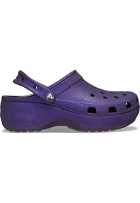Lila Clogs mit glatter, strukturierter Oberfläche, die über Belüftungsöffnungen, einen Riemen hinten und eine dicke Plattformsohle für mehr Höhe verfügen.