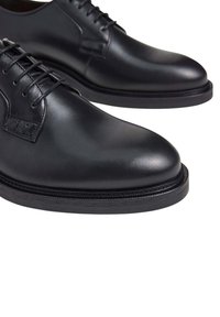 Scarpe da dress in pelle nera con finitura liscia, punta arrotondata e design tradizionale con lacci. Presentano una suola stratificata con accenti testurizzati.
