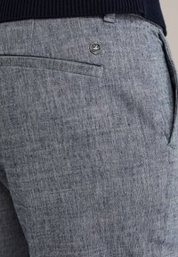 Šviesiai mėlynos tekstūruotos kelnės su mažu metaliniu logotipu ant galinio kišenės ir subtiliais siuvimo detalėmis.