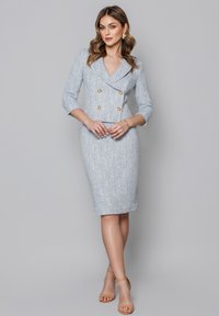 Jasnoniebieska, dopasowana sukienka z teksturowanej tkaniny, w stylu marynarki podwójnie zapiętej, z rękawami o długości trzech ćwiartek oraz złotymi guzikami.