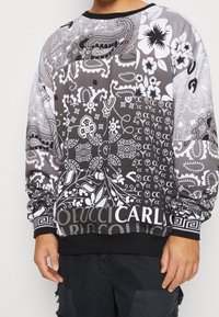 Černobílá mikina s květinovými a paisley vzory, žebrovaným kulatým výstřihem a elastickými manžetami, s nápisem "CARLO" na lemu.