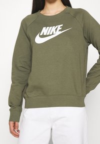 Olivgrön sweatshirt tillverkad av bomullsmix, med en framträdande vit Nike-logotyp över bröstet samt ribbade mudd och nederkant.