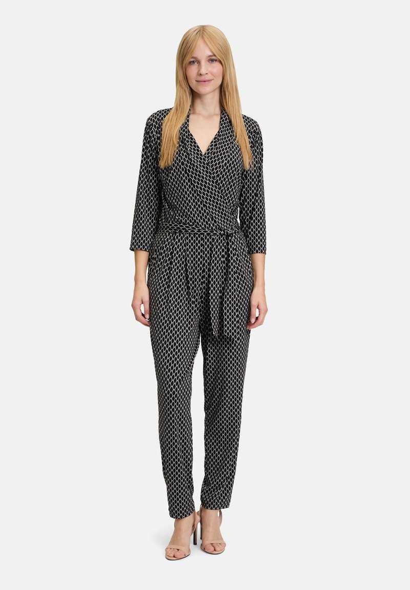 Svart och vit mönstrad jumpsuit med knytdesign, långa ärmar, midjebälte och avsmalnande ben, tillverkad av ett lätt tyg.