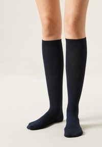 Calcetines azul marino hasta la rodilla con una textura suave, hechos de un material elástico y ligero. Presenta un puño acanalado en la parte superior.