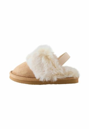 Beiger Wildleder-Hausschuh mit dicker weißer flauschiger Fellfütterung und einem elastischen Riemen hinten auf einer Gummisohle, seitlich dargestellt.