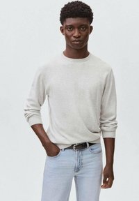 Hellgrauer Strickpullover mit langen Ärmeln und Rundhalsausschnitt; kombiniert mit hellblauen Jeans aus Denim. Der Pullover hat gerippte Bündchen und Saum.