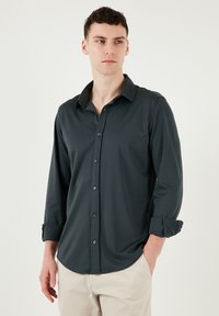 Donkergrijze lange mouwen shirt van soepel fabric met een kraag, knoopsluiting aan de voorkant en opgerolde mouwuiteinden. Eenvoudig ontwerp zonder patronen.