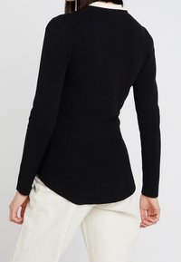 Czarna bluzka z długim rękawem o dopasowanym kroju, z okrągłym dekoltem i zaokrąglonym dołem. Wykonana z gładkiej tkaniny z lekkim stretchu.
