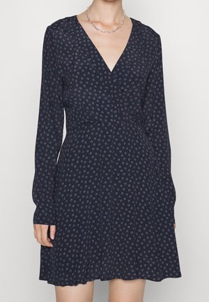 Sukienka w kwiatowy wzór w ciemnym granacie, z długimi rękawami, głębokim dekoltem w kształcie litery V i rozkloszowanym dołem. Wykonana z lekkiej tkaniny o gładkiej fakturze.