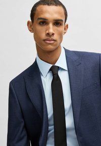Giacca uomo blu navy con motivo testurizzato sottile, abbinata a una camicia dress leggera blu chiaro e una cravatta nera, con un design del colletto classico.