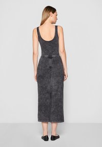 Rochie midi gri cu spatele decupat, realizată dintr-un material texturat. Prezintă o talie accesorizată cu un brâu și o deschidere la spate pentru a facilita mișcarea.