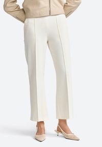 Pantalons crème, taille mi-haute avec des plis à l'avant, design à jambe large, texture lisse, associés à des chaussures slingback beiges à bout pointu.