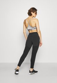 Sujetador deportivo en gris con efecto tie-dye y tirantes finos, combinado con pantalones negros ajustados con bolsillos y una cinturilla elástica. Zapatillas deportivas negras.