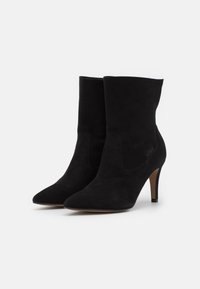 Černé semišové ankle boty s špičatou špičkou a jehlovým podpatkem. Mají hladkou texturu a elegantní design s viditelnými švy.