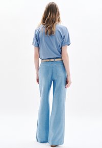 Ljusblå vida jeans med bakfickor, som är kombinerade med en kortärmad blå topp med upprullade ärmar och ett beige bälte. Slät denimtextur.