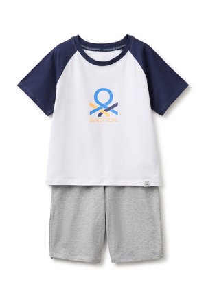 Chemise blanche à manches courtes avec manches bleu marine et logo, associée à un short gris clair, posée à plat sur fond blanc.