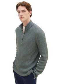 Texturiertes grünes Pullover mit Viertelreißverschluss und Stehkragen, mit einem gewobenen Muster und langen Ärmeln, kombiniert mit einer cremefarbenen Innenlage.