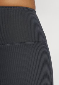 Leggings noirs côtelés avec une large taille, présentant une surface texturée et des coutures à plat pour le confort et l'élasticité.