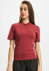 Rød t-shirt med korte ærmer og ribbet rund hals. Har hvid tekst "Thug Life" på skulderen og siden, lavet af en glat bomuldsblanding.