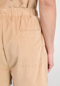 Pantalons en velours côtelé beige avec une taille élastique, présentant une seule poche arrière et une texture côtelée. Gros plan sur le tissu et le détail de la pochette.