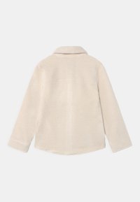 Beige fleece jacket with a collar, long sleeves, and a soft texture. Features a rounded hem and a square label on the upper back.