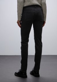 Slim-fit, tmavě šedé džíny s zadními kapsami, měkkou texturou a středním pasem, spárované s černými šněrovacími botami.