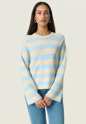 Lys blå og krème stribet sweater med ribbet tekstur, bådudskæring og brede, svajende ærmer. Kombineret med denim jeans.