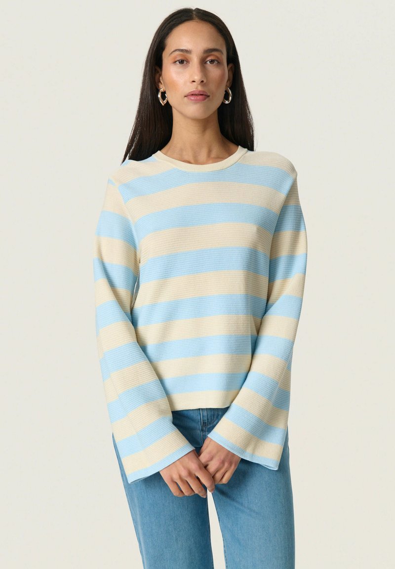 Lys blå og krème stribet sweater med ribbet tekstur, bådudskæring og brede, svajende ærmer. Kombineret med denim jeans.