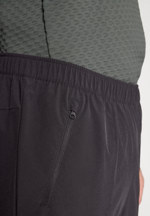 Black athletic shorts with elastic waistband, featuring a zippered pocket on the side and layered over a textured green top.