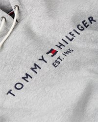 Pilka medvilninė džemperis su stringais ant gobtuvo, siuvinėtas "TOMMY HILFIGER" logotipas tamsiai mėlyna spalva ir įsteigimo data "EST. 1985" pilka spalva.