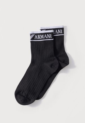 Para czarnych prążkowanych skarpetek za kostkę z białym paskiem na górze, na którym znajduje się napis „ARMANI” oraz logo w białym kolorze.