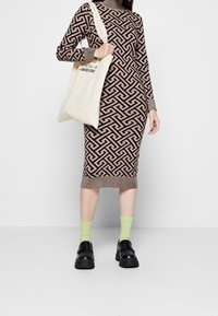 Abito di maglia marrone con motivo geometrico, colletto a vulcano a coste e orlo; abbinato a scarpe con piattaforma nere e calze verde chiaro; borsa a tracolla in tela.
