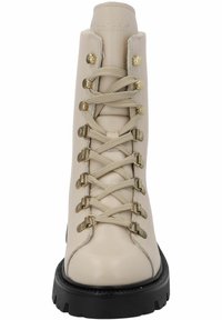 Botín de cuero beige con cordones, herrajes en tono dorado, suela acanalada, parte superior texturizada y detalle de cordones entrecruzados. Diseñado para la durabilidad.