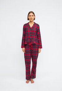 Rødrutete pysjamassett som inkluderer en knapp-opp skjorte med krage og lange ermer, kombinert med bukser med snøring. Mykt stoff med rutete mønster.