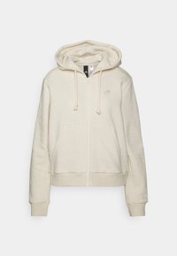 Krémová mikina na zip s předními kapsami, kapucí na šňůrku a jemným logem Adidas na hrudi a manžetě, vystavená na bílém pozadí.