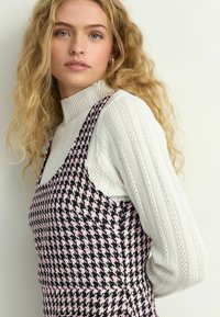 Melna un rozā houndstooth raksta kleita, pārklāta ar baltu, ribotu krekla ar garām piedurknēm un augstu kaklu. Iespējas plānas siksniņas un pieguloša dizaina.