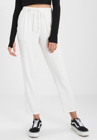 Pantalon en lin blanc avec une taille élastique et un cordon de serrage, présentant un design à jambes droites. Assorti à des baskets noires.