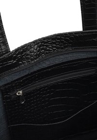Borsa a tracolla nera con una texture a motivo coccodrillo. Presenta tasche interne con zip e dettagli in pelle liscia. Doppi manici.