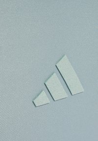 Tela texturizada azul claro con un logotipo prominente de tres rayas en un azul ligeramente más oscuro, con un acabado mate y elementos de diseño geométrico.