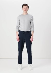 Grau langärmliges Shirt und marineblaue Hose, aus weichem Stoff gefertigt. Die Hose hat einen Kordelzugbund und tapered Bein, kombiniert mit weißen Sneakern.