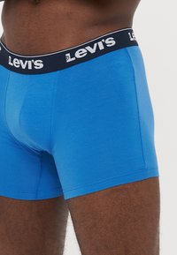 Boxeri din bumbac albastru cu un brâu elastic negru, având logo-ul alb "Levi's". Textură netedă, cu un design ajustat și fără modele vizibile.